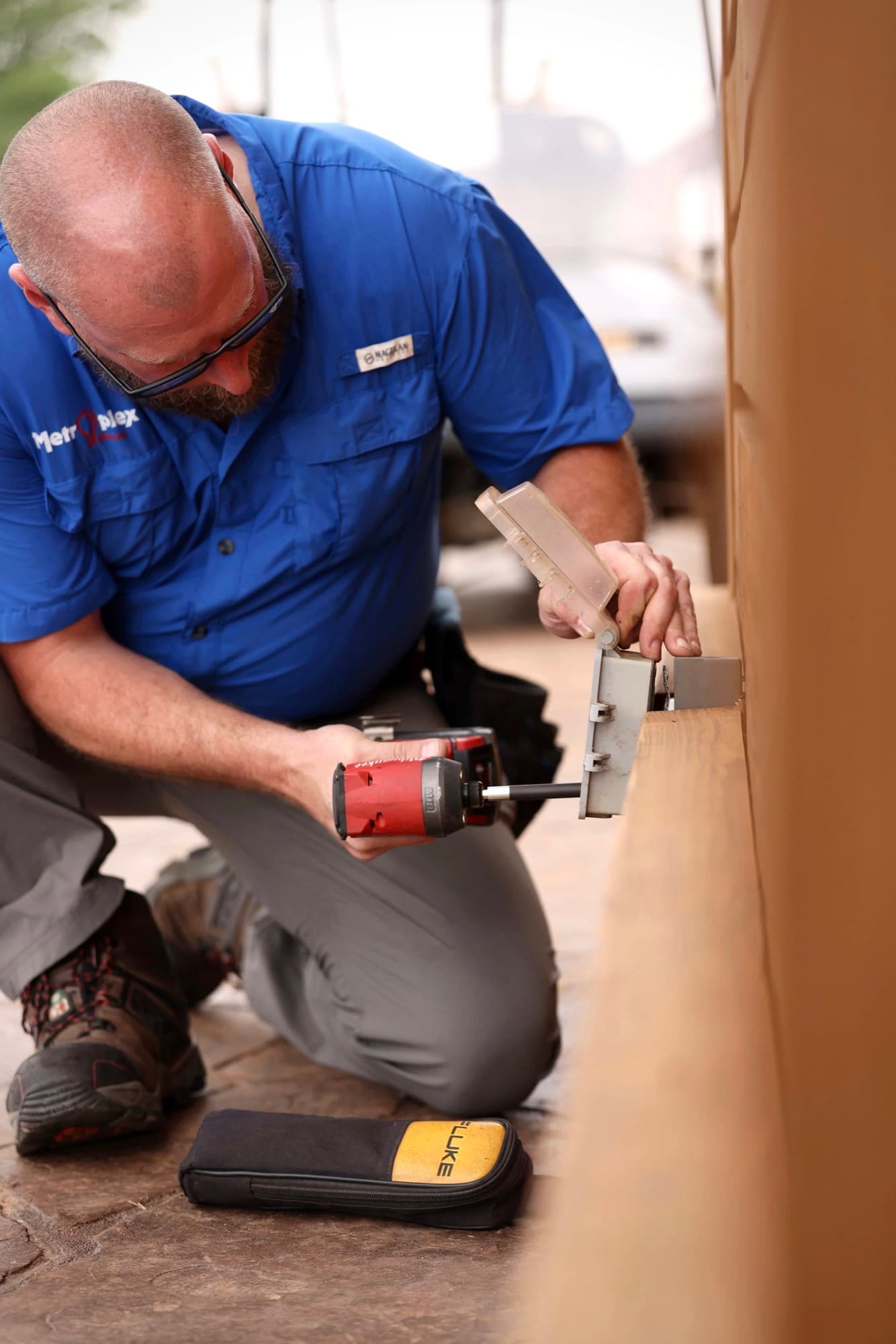 A Metroplex technician kneeling to mount equipment on an exterior wall