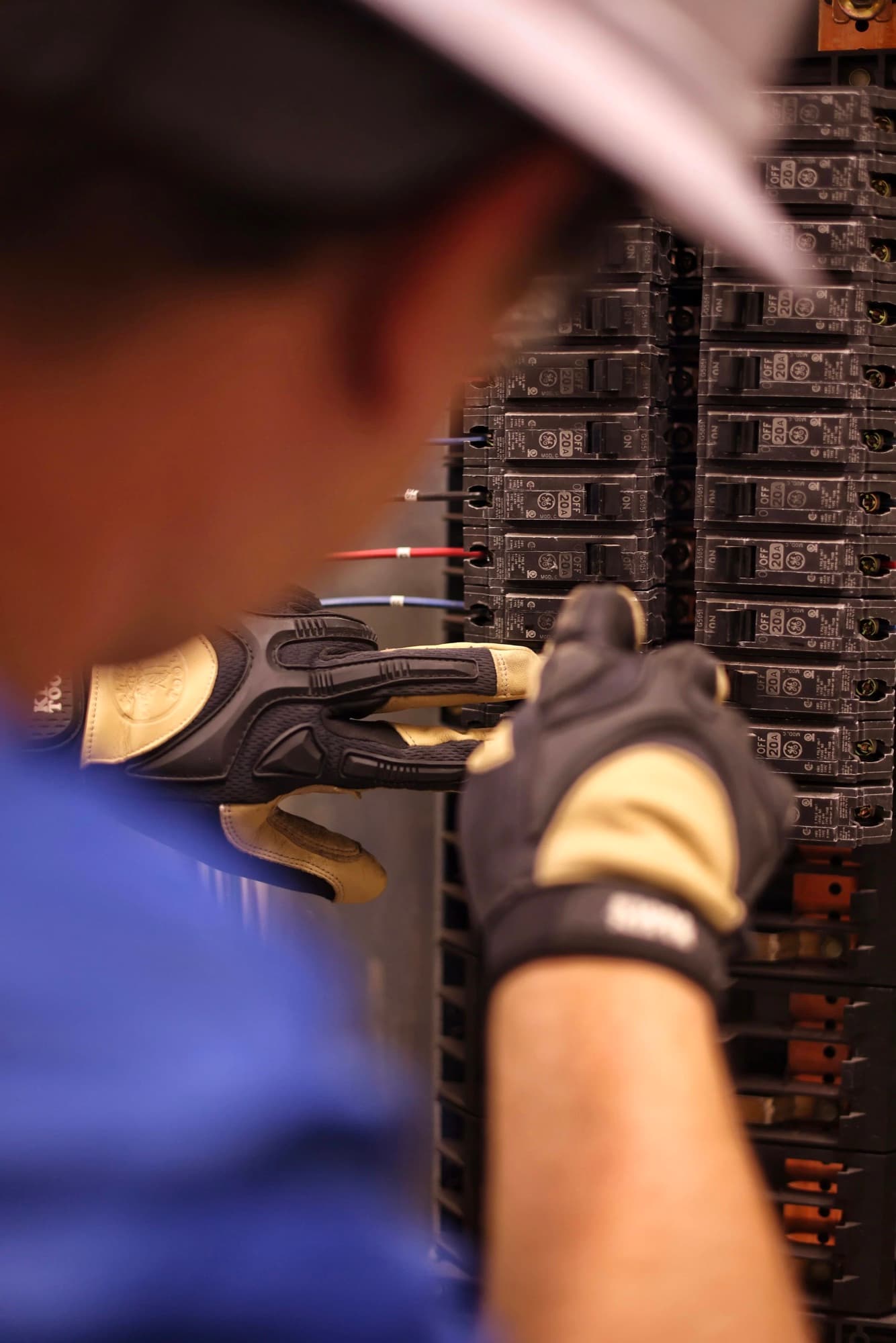 A gloved Metroplex electrician wiring a breaker panel